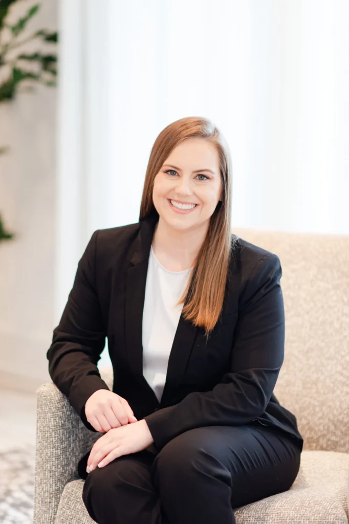 Whitney Goulish, President & Founder in Black Suit Sitting on Tan Chair