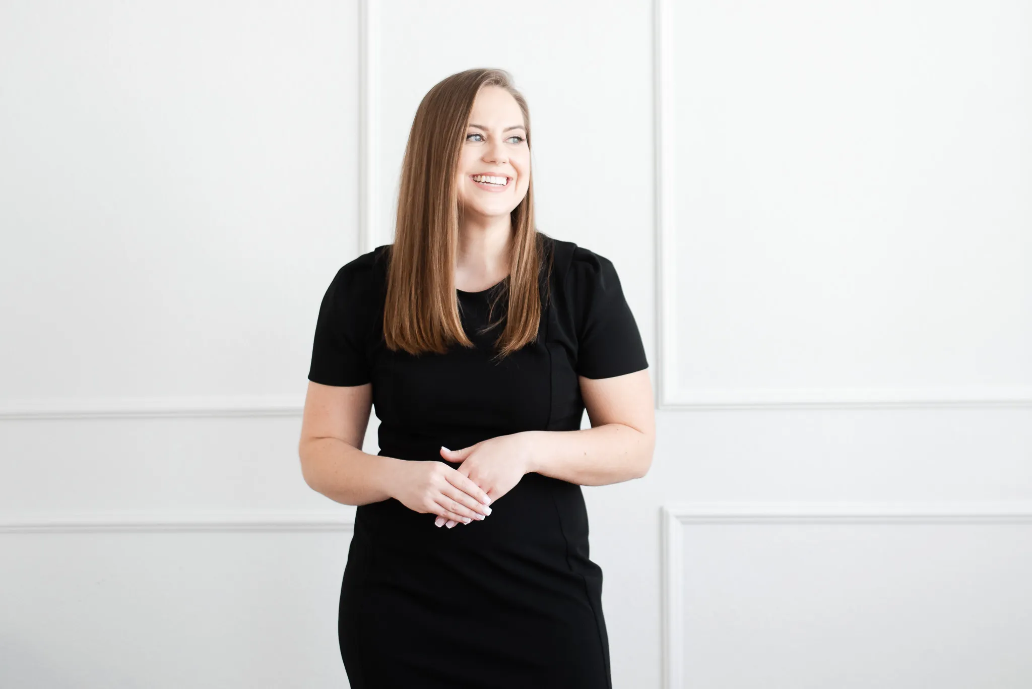 Whitney in Black Dress Standing in Front of White Wall