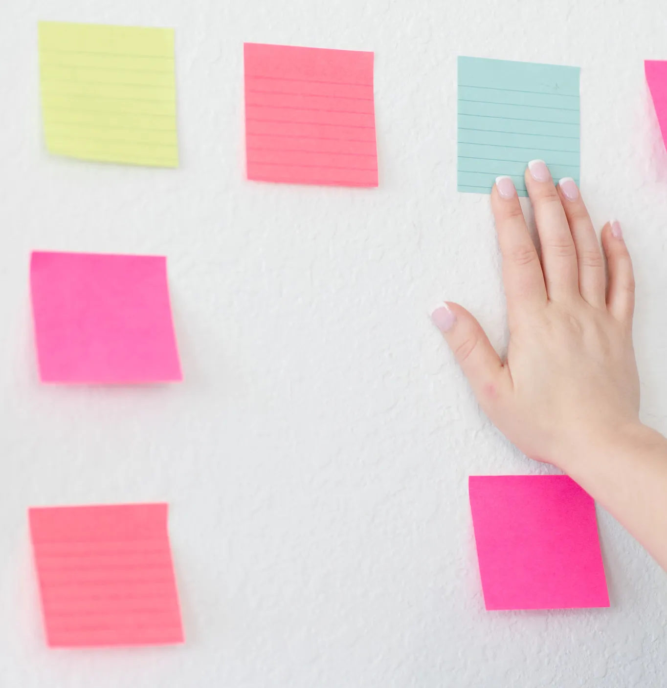 Hands Aligning Different Colored Sticky Notes on a Wall