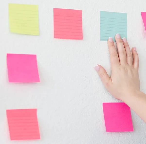 Hands Aligning Different Colored Sticky Notes on a Wall
