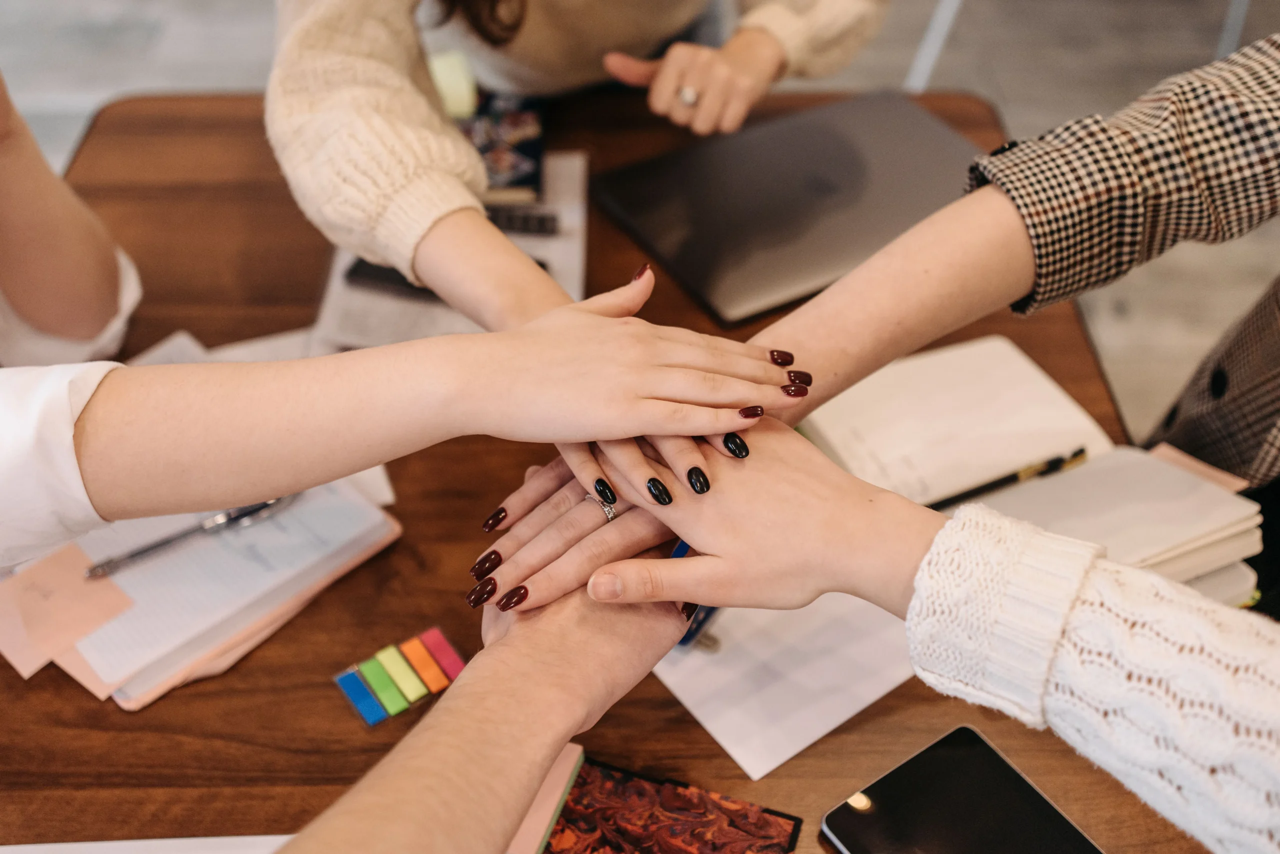 Hands Stacked in Teamwork Gesture Over Table Hands Stacked in Teamwork Gesture Over Table