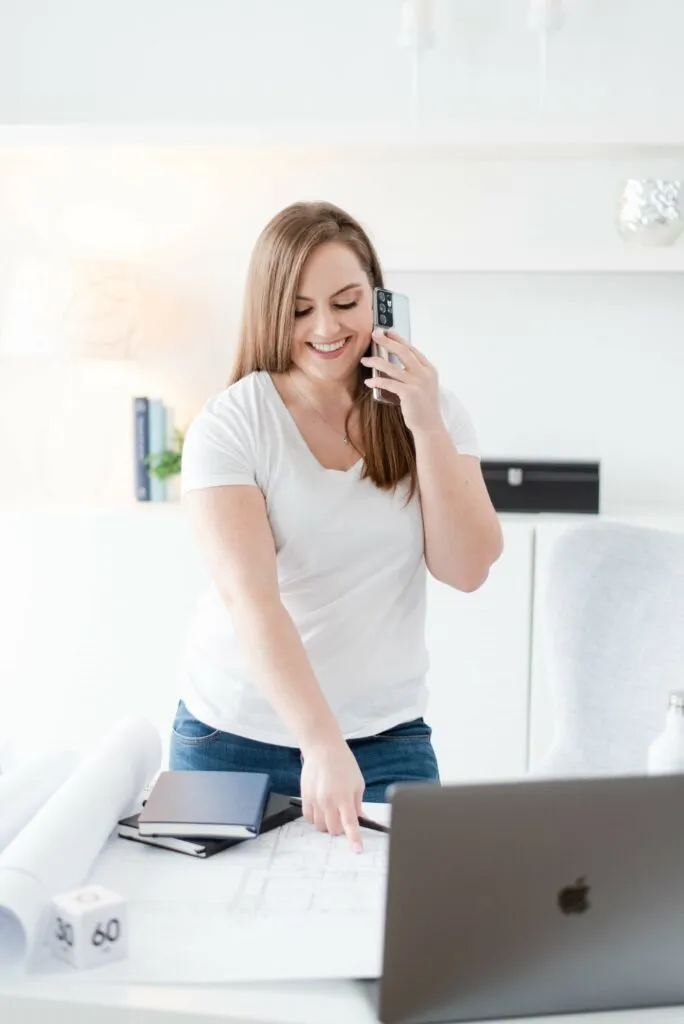 Whitney in White Standing Over Desk While on Phone