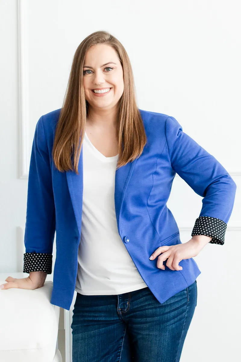 Whitney in Blue Jacket Standing by White Chair